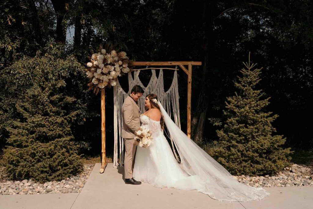 Outdoor boho wedding ceremony with a macrame-decorated arch and dried pampas grass floral arrangements.