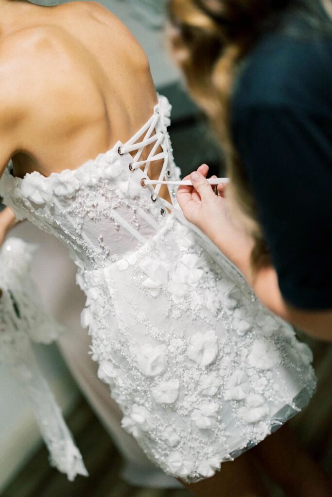 Close-up of a bridal gown with intricate lace-up detailing and floral embellishments, showcasing the dress's elegant design and texture.