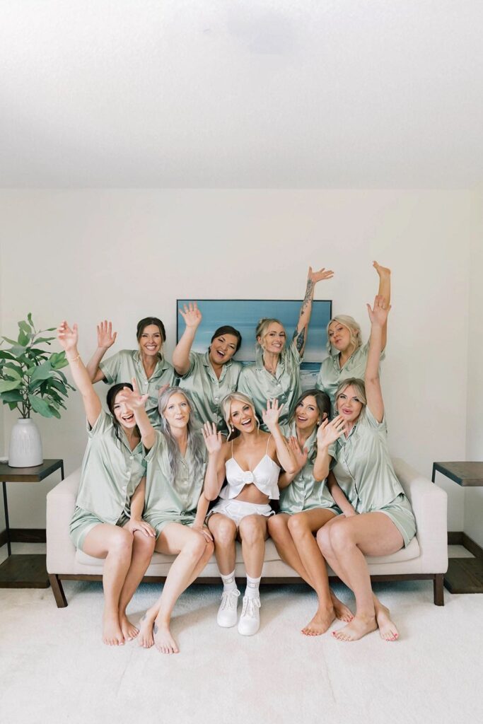 Bridal party celebrating with joy, all dressed in matching satin robes and gathered together on a cozy sofa at The Pines venue.