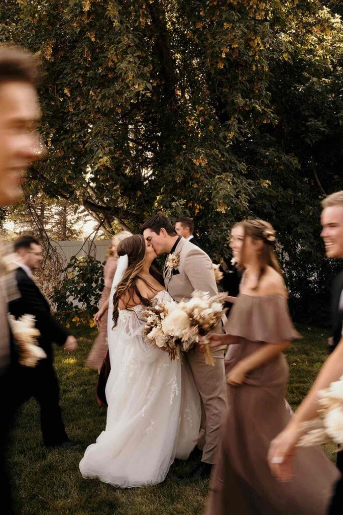 Bride and groom sharing a kiss surrounded by blurred motion of the wedding party in elegant neutral tones.