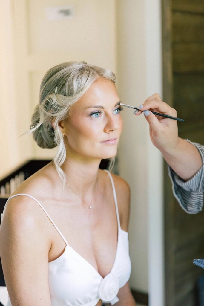 Bride being pampered with makeup and hair styling before the wedding ceremony at The Pines venue, capturing a moment of calm before the celebration.