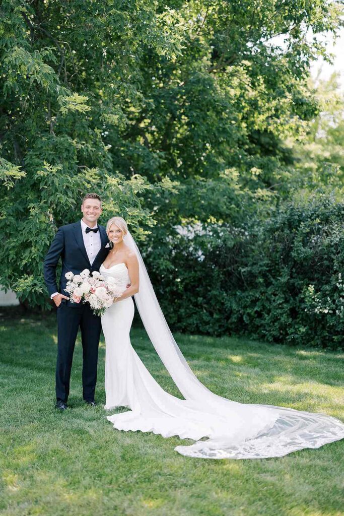 Bride and groom posing together in a serene moment, with the bride’s long veil flowing gracefully in the background of the lush outdoors at The Pines.
