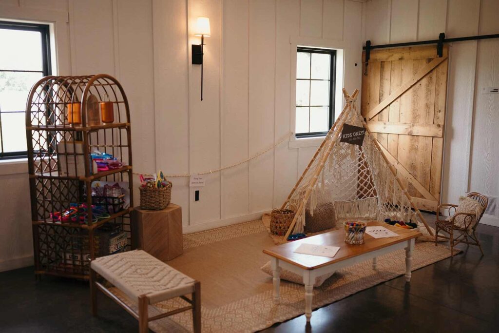 A designated kids’ play area featuring a macramé teepee, small chairs, toys, and a rattan shelf filled with colorful items. The space is styled with boho-inspired decor.