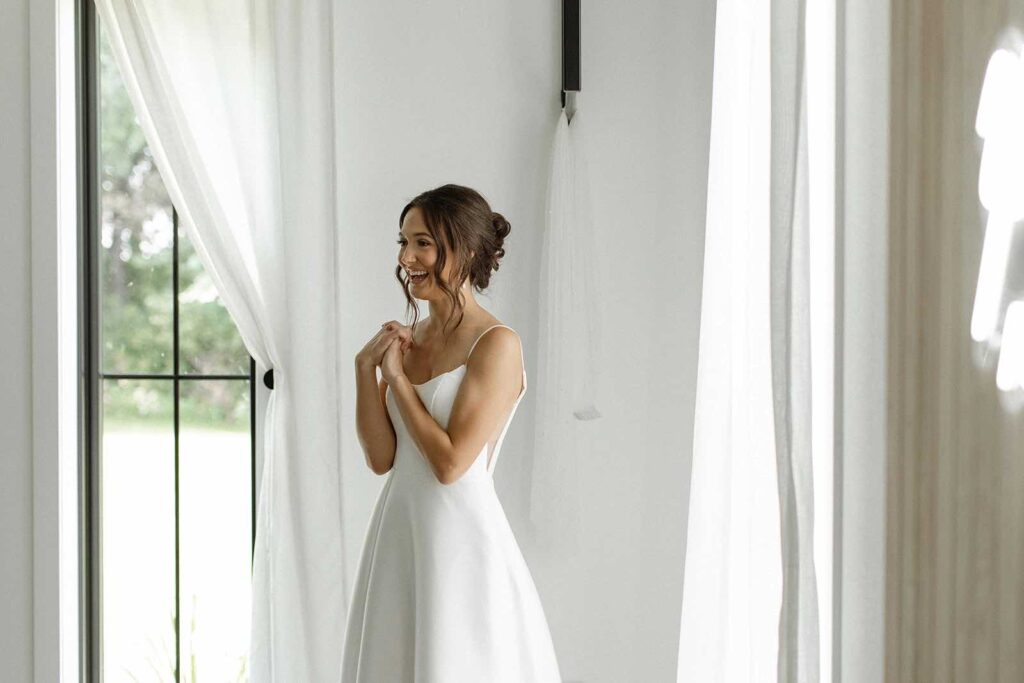 Bride, glowing and smiling, in her wedding dress during her getting-ready moment