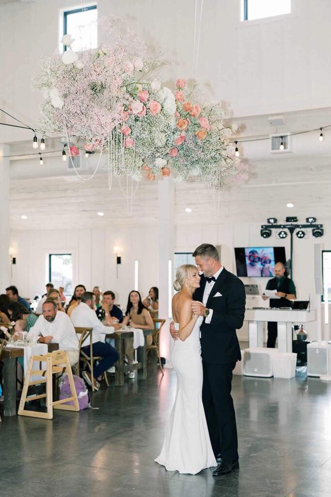 The bride and groom share a joyful first dance at The Pines, twinkling lights above and loved ones surrounding them.