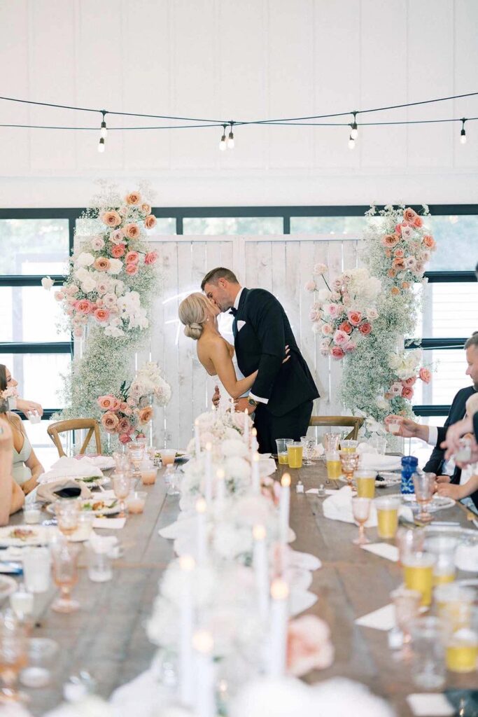 A bride and groom share a kiss behind their head table during their reception inside pines white.