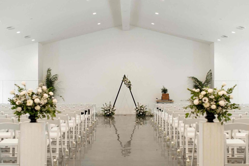 Modern wedding ceremony setup at The Pines featuring a triangular arch with white and green florals