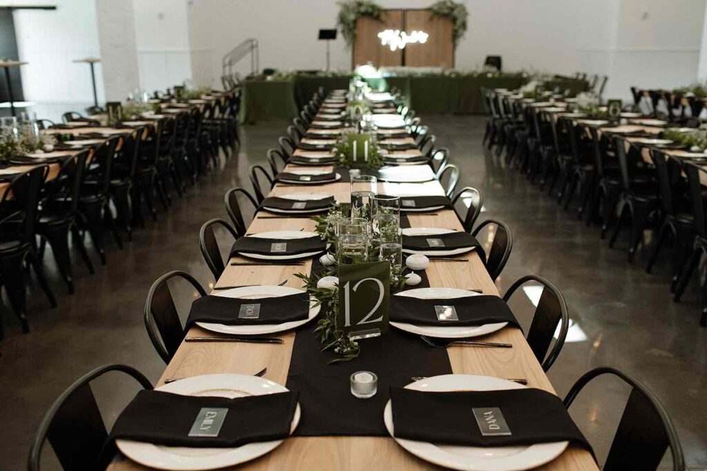 Modern reception tablescape at The Pines with black table settings, greenery, and natural wood tables.