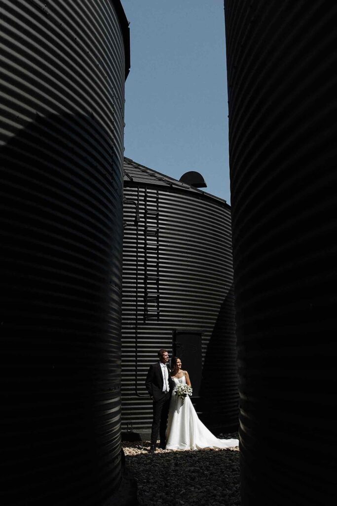 Unique couple portrait standing between black grain silos, blending modern and rustic vibes
