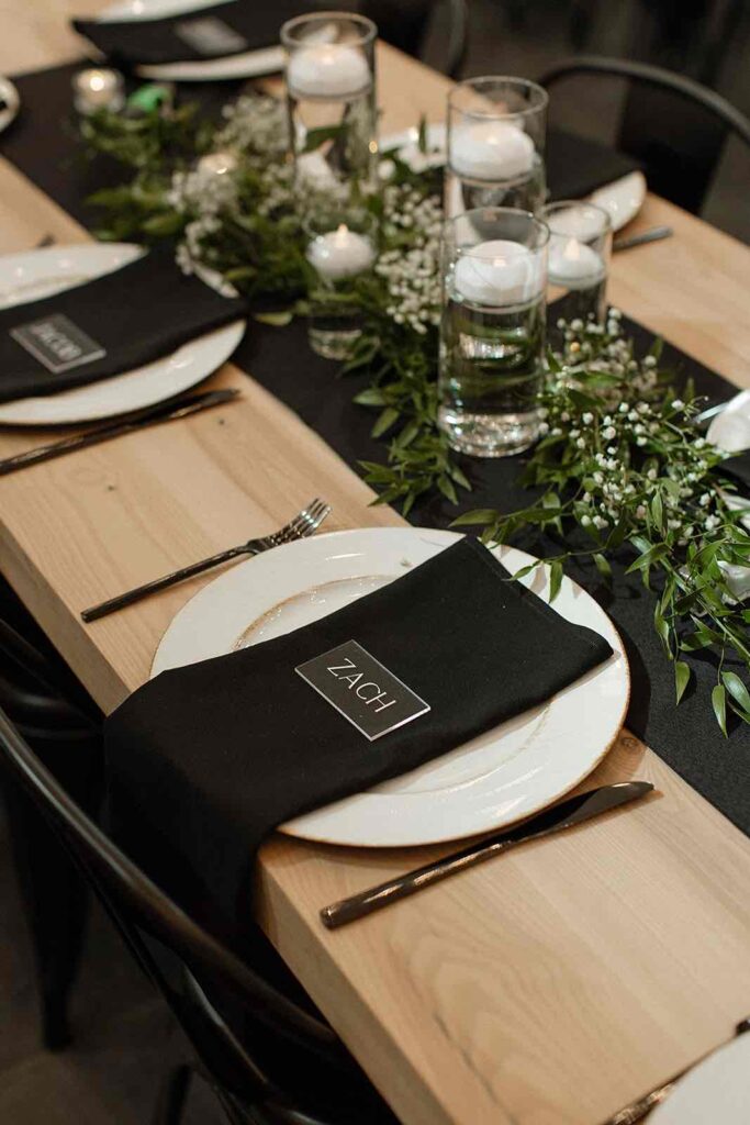 Reception table settings at The Pines with black napkins and gold-rimmed white plates, personalized for each guest
