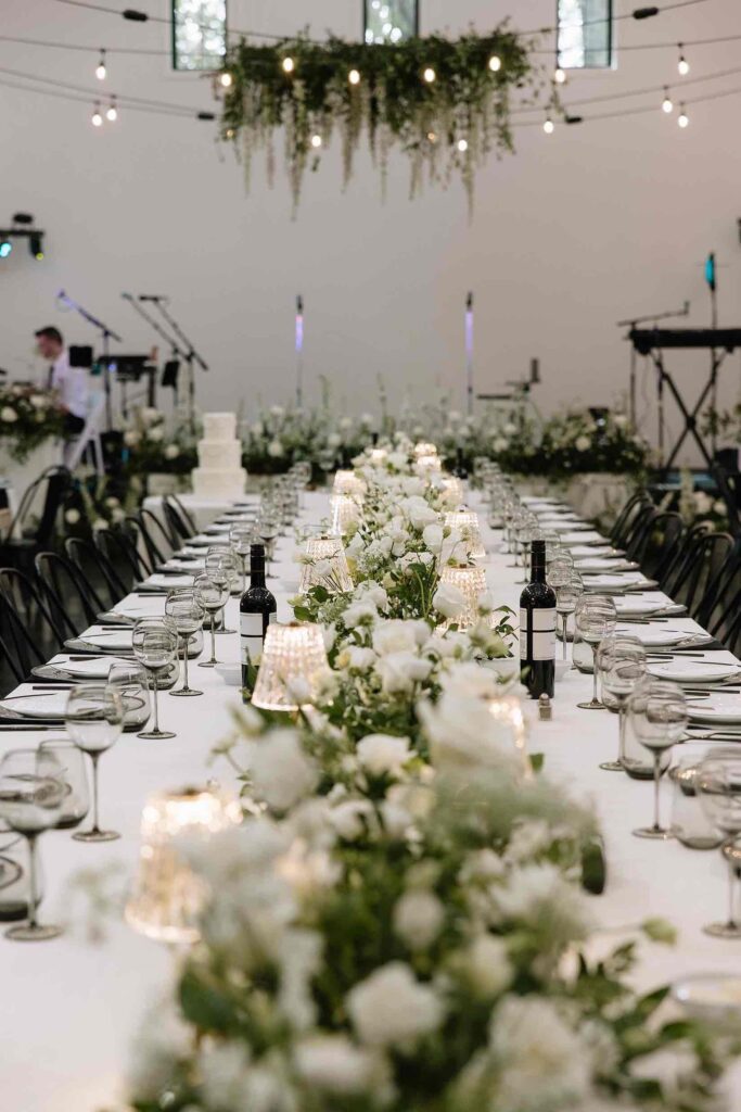 Beautifully decorated wedding head table at The Pines, with cascading white floral arrangements, candles, and black chairs creating a luxurious setting.