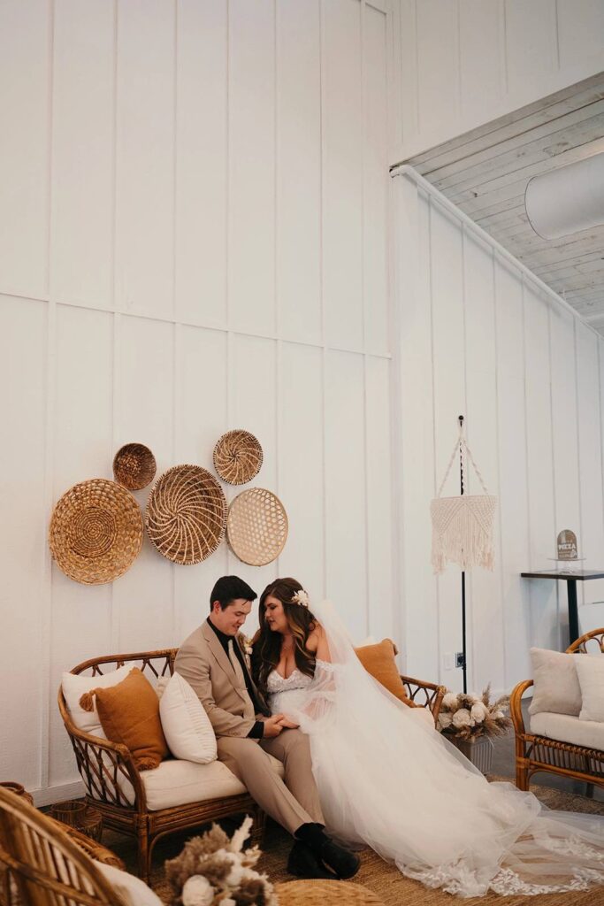 Bride and groom sitting on their boho wedding reception soft seating section during their wedding reception.