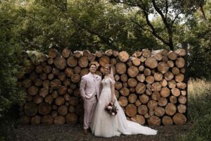 Bride and groom posing in front of a log wall at The Pines Wedding Venue.