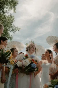 Bride surrounded by her bridesmaids holding parasols and pastel florals during an outdoor summer wedding