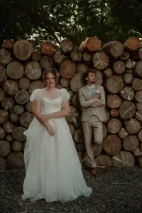 Editorial wedding portrait of bride and groom standing by a rustic woodpile
