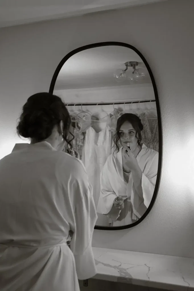 Bride applies lipstick in front of a mirror while getting ready in the bridal suite