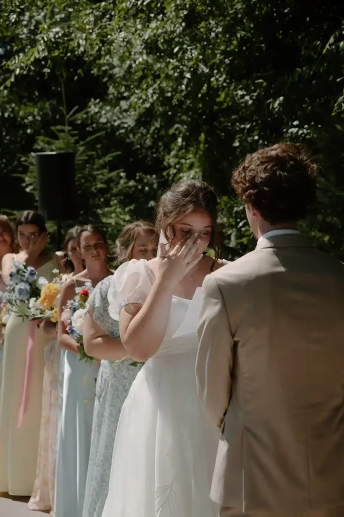 Emotional bride reads her vows during a summer outdoor ceremony surrounded by bridesmaids