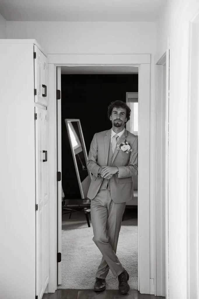 black and white groom portrait leaning in door frame