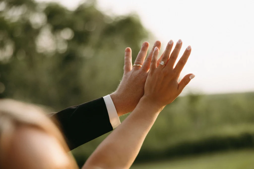 bride and groom hand with rings on over field for photo after getting married